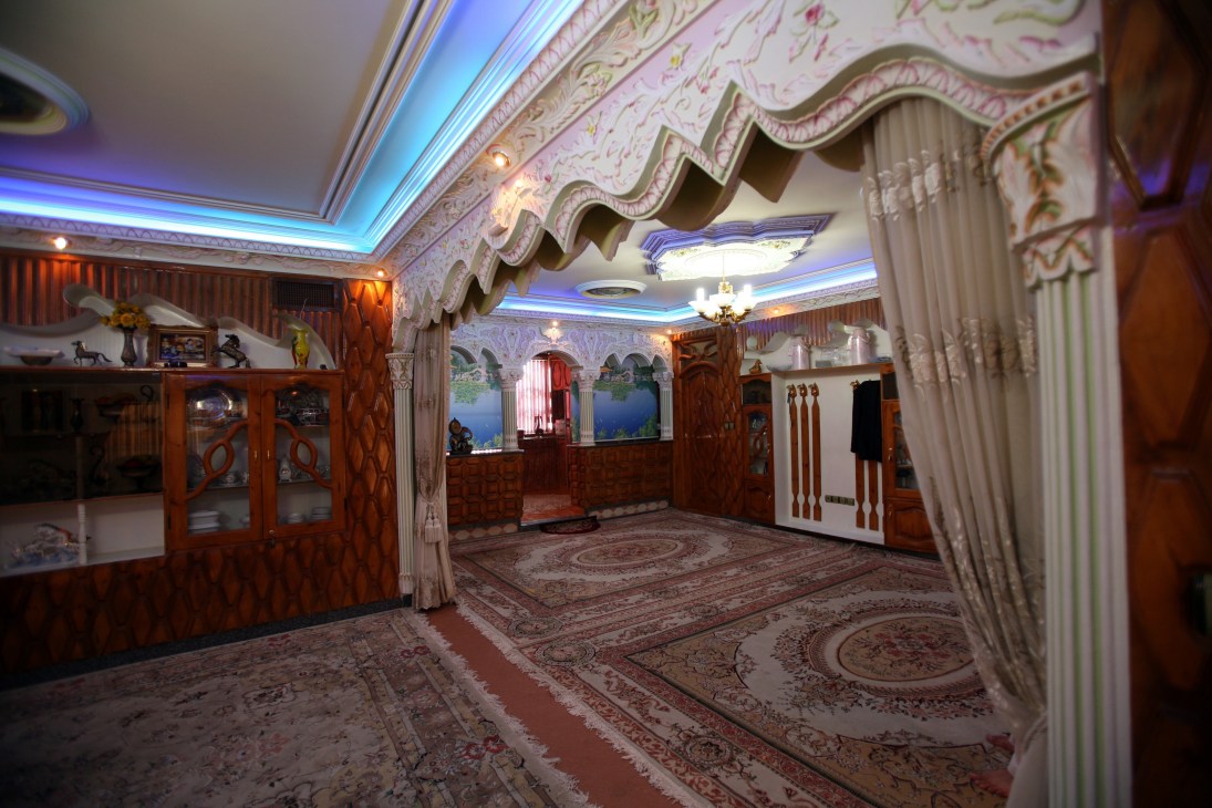 Ornate sitting room with pink patterned ceiling, wood paneling, Persian carpets, and blue fluorescent lighting fixtures.
