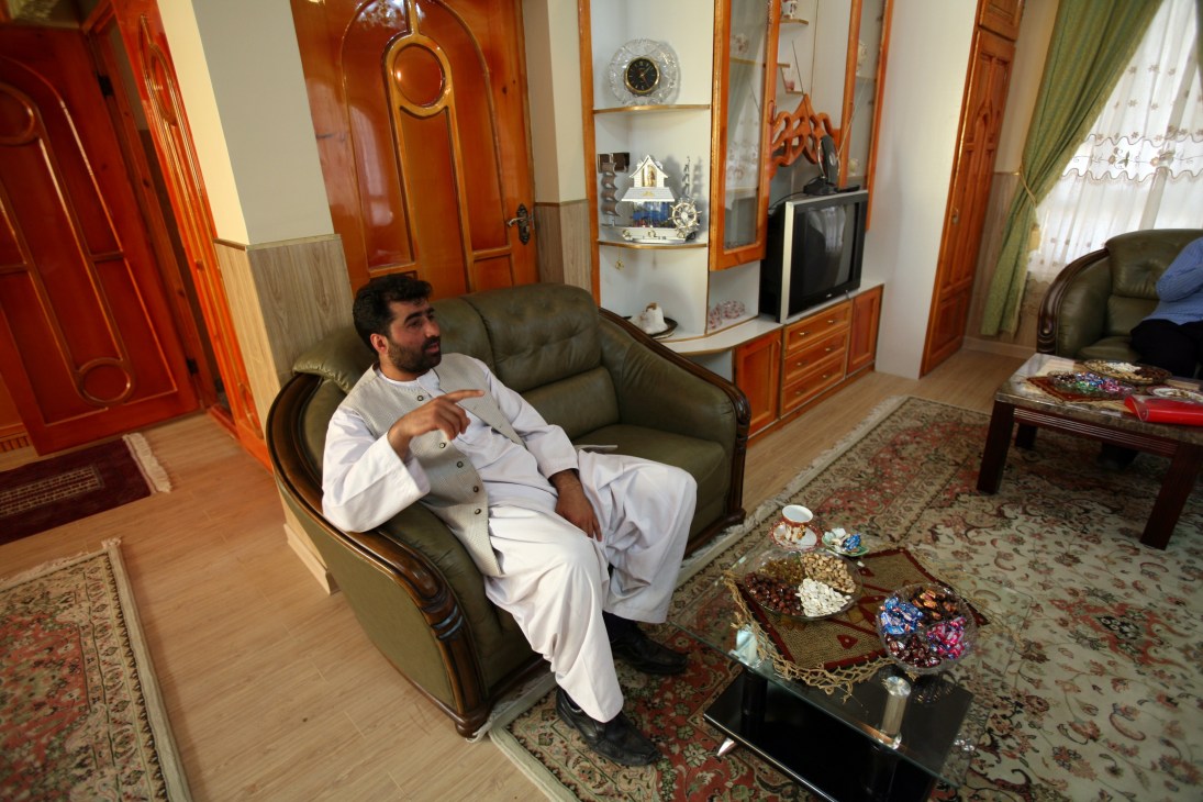 Habibullah Nasiri relaxes on a leather sofa in an ornate sitting room with red wooden doors and decorative shelving.