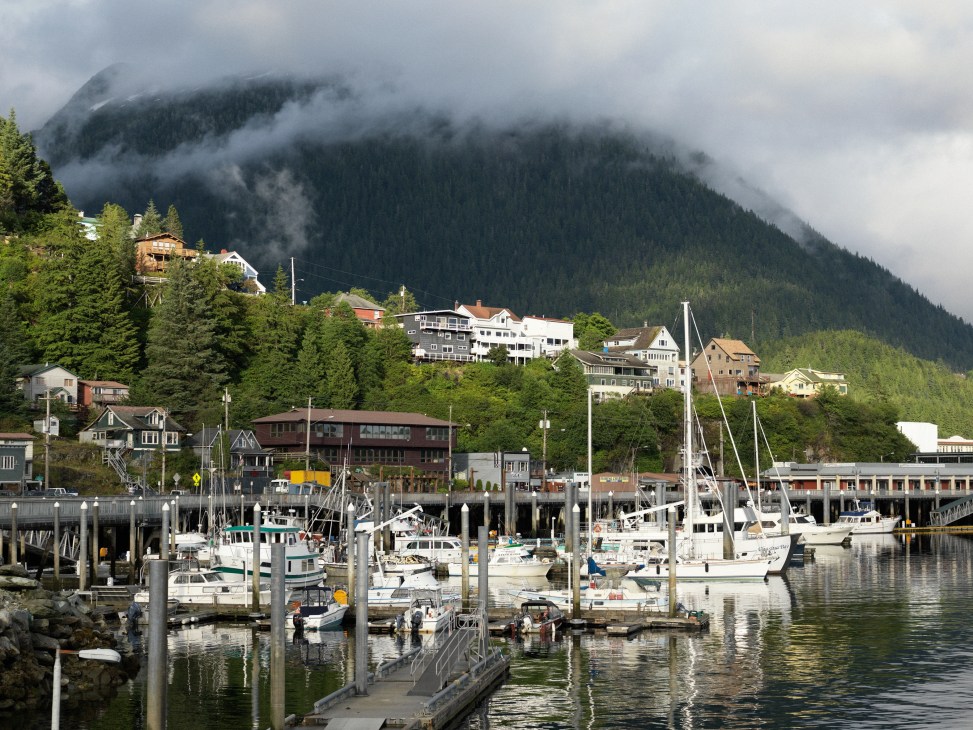 Ketchikan's waterfront with houses built on hillside above boat harbor, forested mountains in mist behind.
