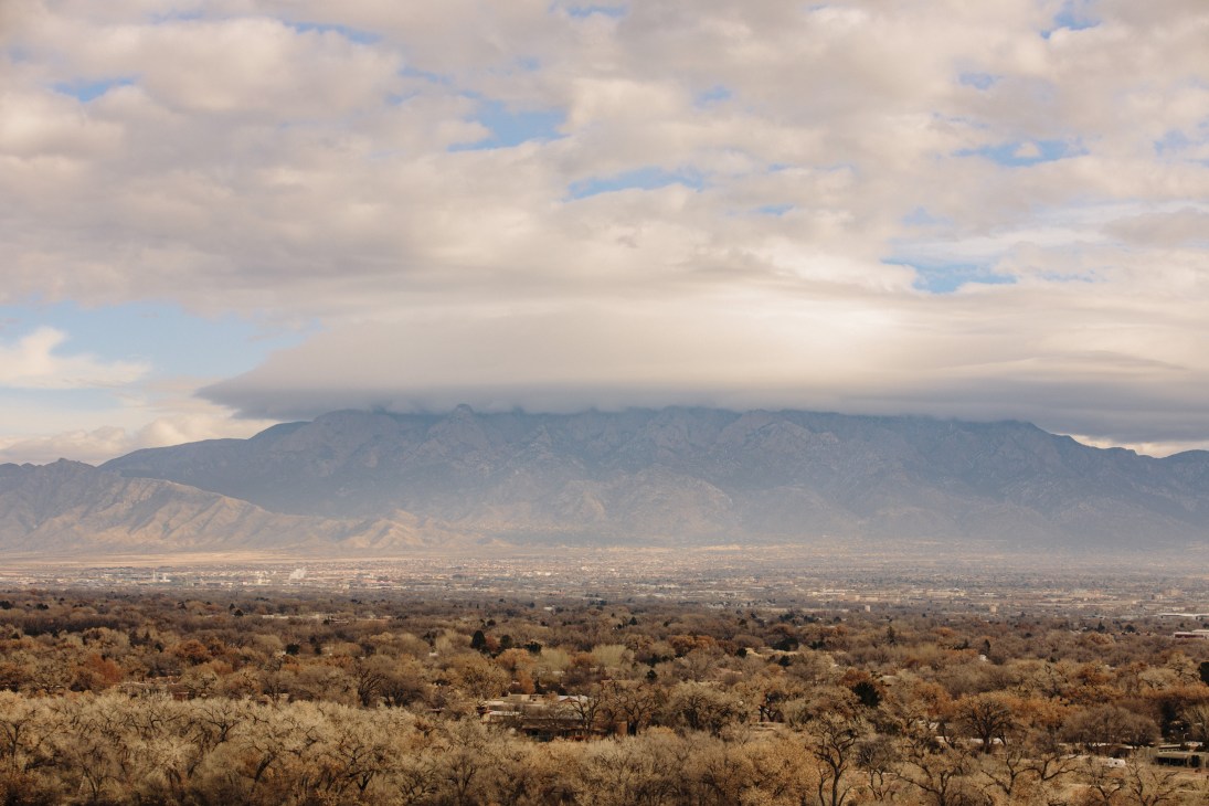 The Sandia Mountains rise above Albuquerque's desert landscape with scattered vegetation in the foreground.