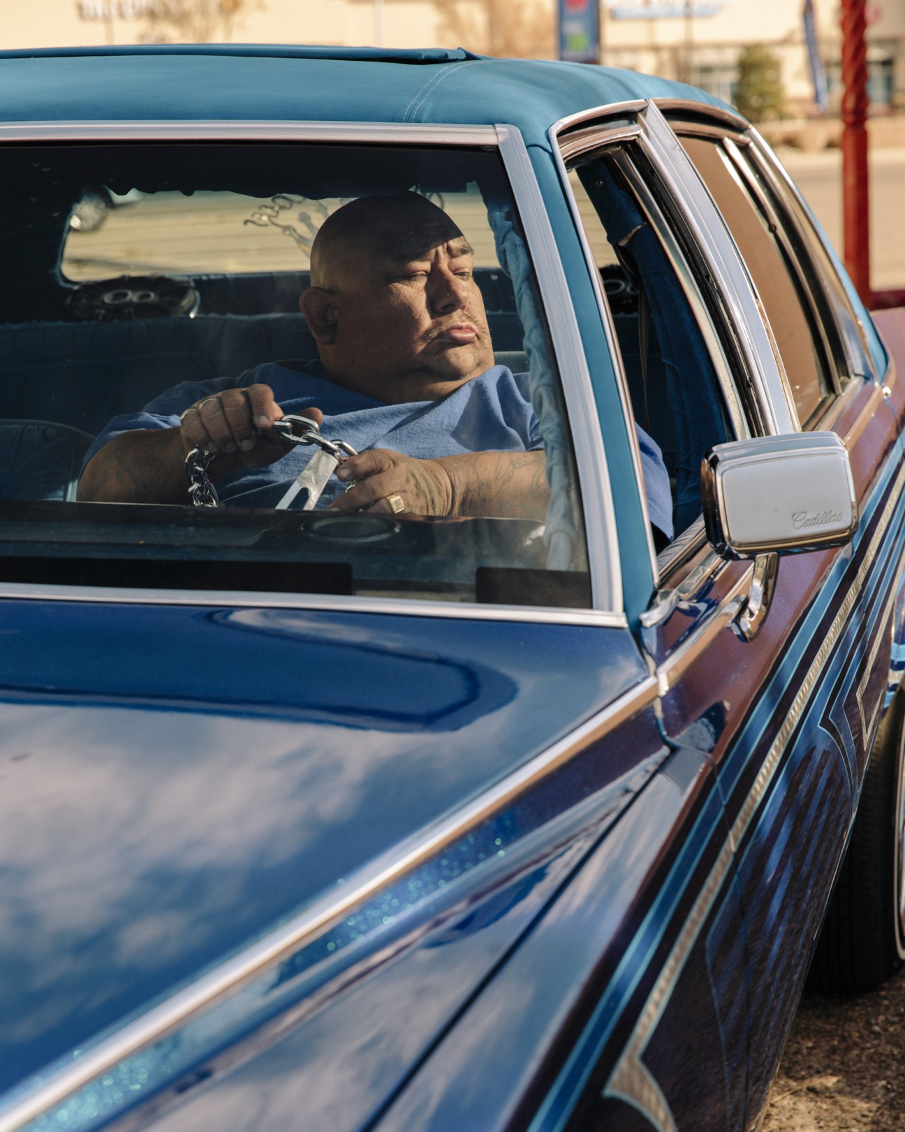 Man sitting in a custom blue low-rider car with polished chrome details and chain steering wheel