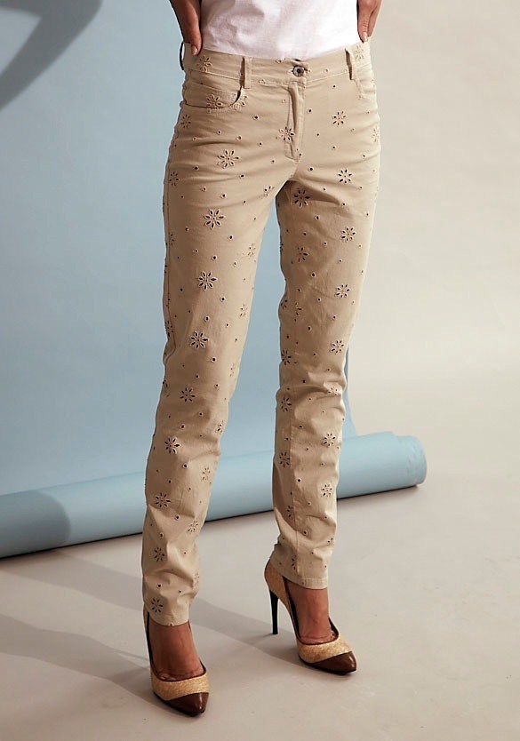 Beige trousers with embroidered floral print worn with brown heeled shoes.