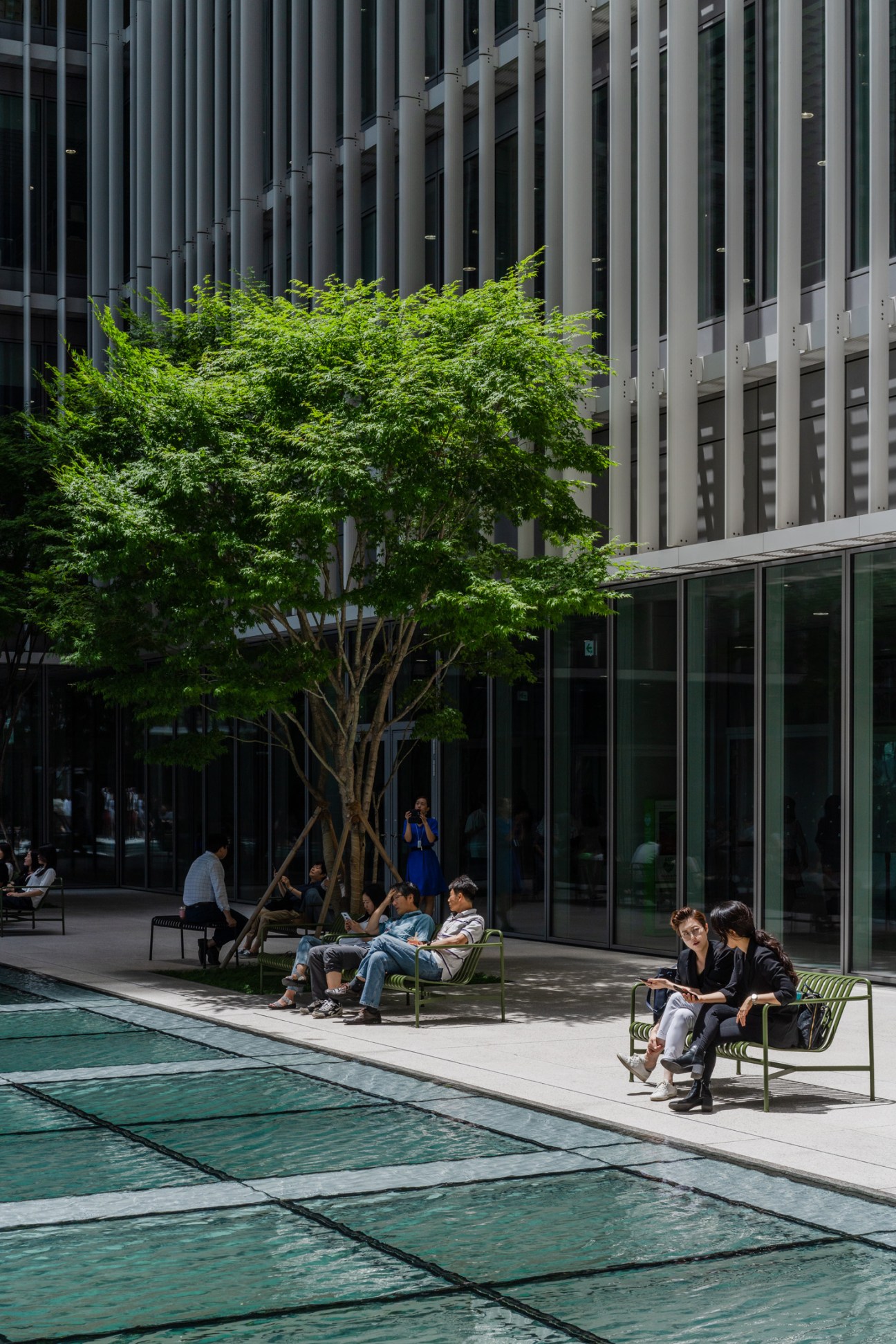 Employees relax on benches beneath a mature tree beside a reflective pool on Amorepacific headquarters terrace.