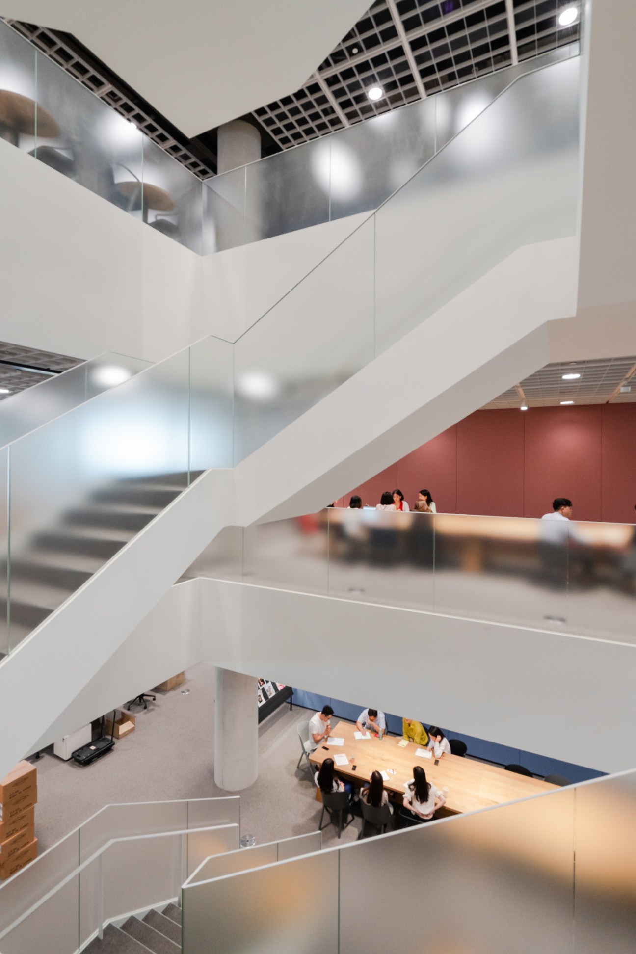 Multi-level interior atrium with curved white stairs, glass railings, and staff working at tables below.