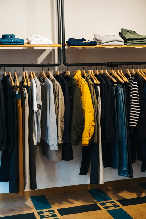 Interior of St Germain menswear shop displaying folded clothing on wooden shelves and garments on wooden hangers along a black rail.