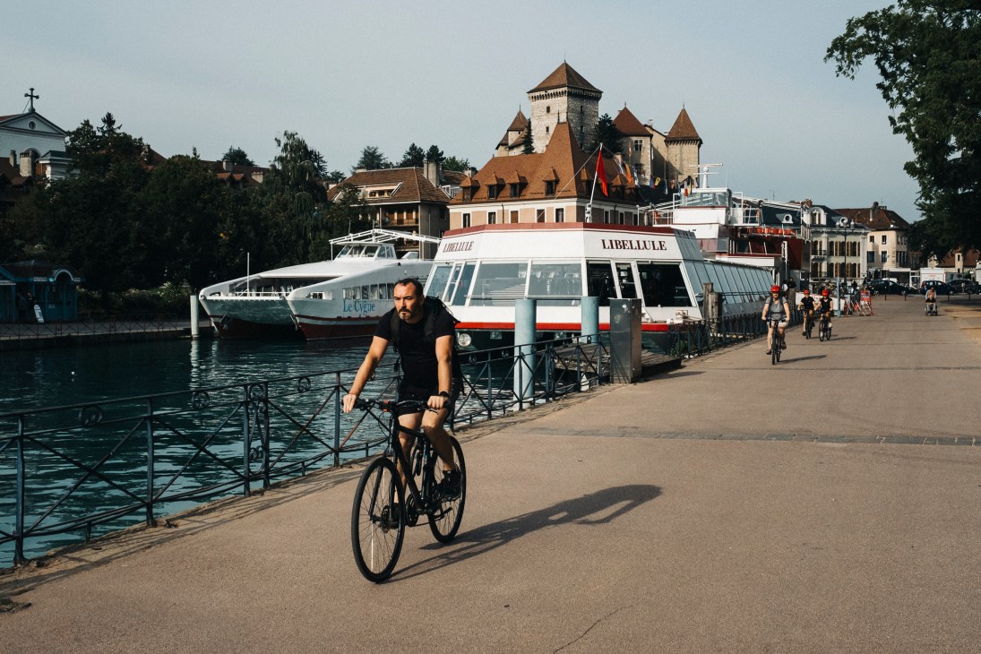 Cyclist riding along Lake Annecy waterfront with historic castle and buildings in background