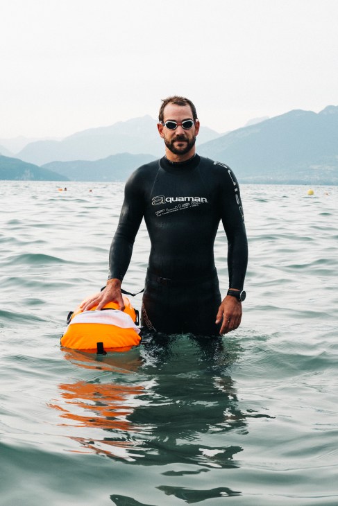 Man in wetsuit wading in lake with mountains in background