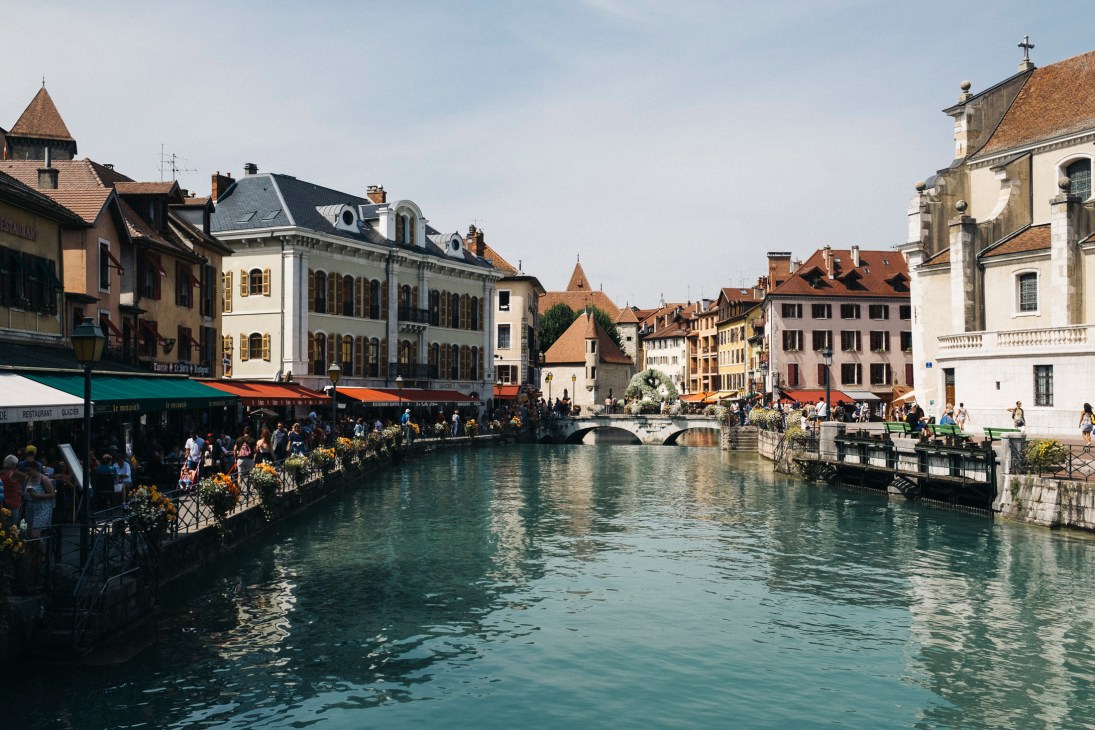 Annecy's old town waterfront with historic buildings, outdoor cafés, and a clear turquoise river flowing through.