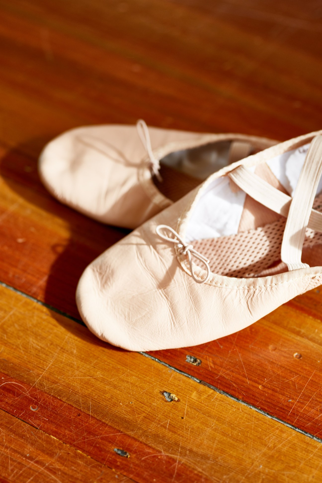Pair of pale pink ballet pointe shoes with ribbons on a wooden floor.