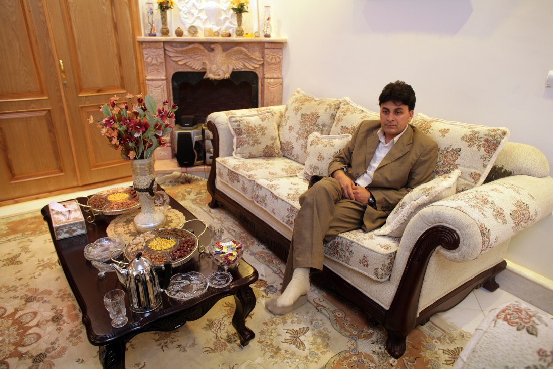 Mohammad Zaher Faqiry sits on a floral patterned sofa in an ornate sitting room with fireplace and decorative objects.