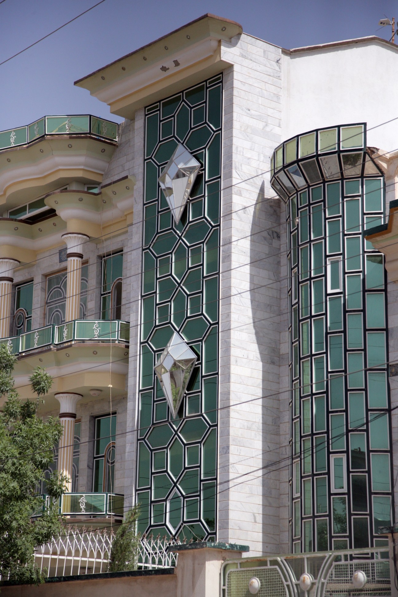 Modern mansion in Herat featuring large mirrored glass diamond-shaped panels on its facade, Corinthian columns, and curved balconies.