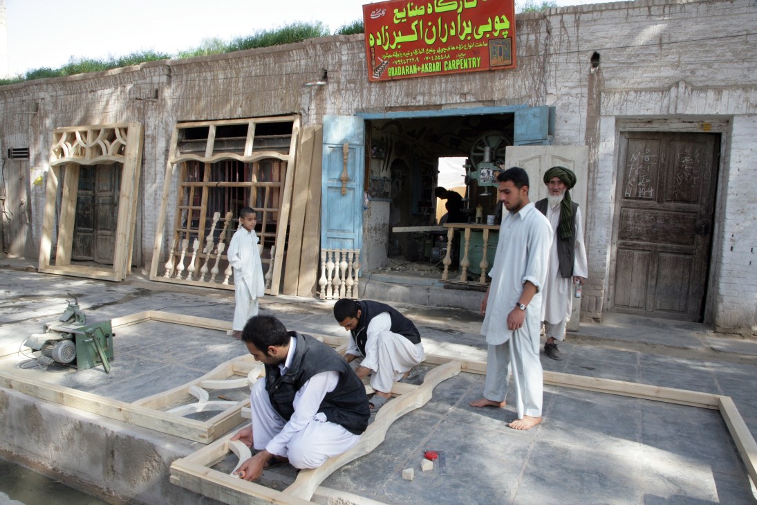 Carpenters work on wooden architectural details in front of a traditional carpentry workshop in Herat.