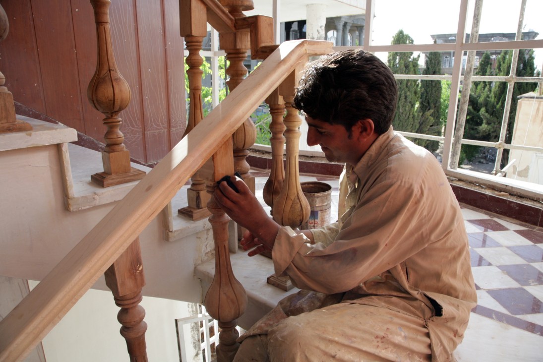 Carpenter staining wooden staircase railings in an ornate entrance hallway