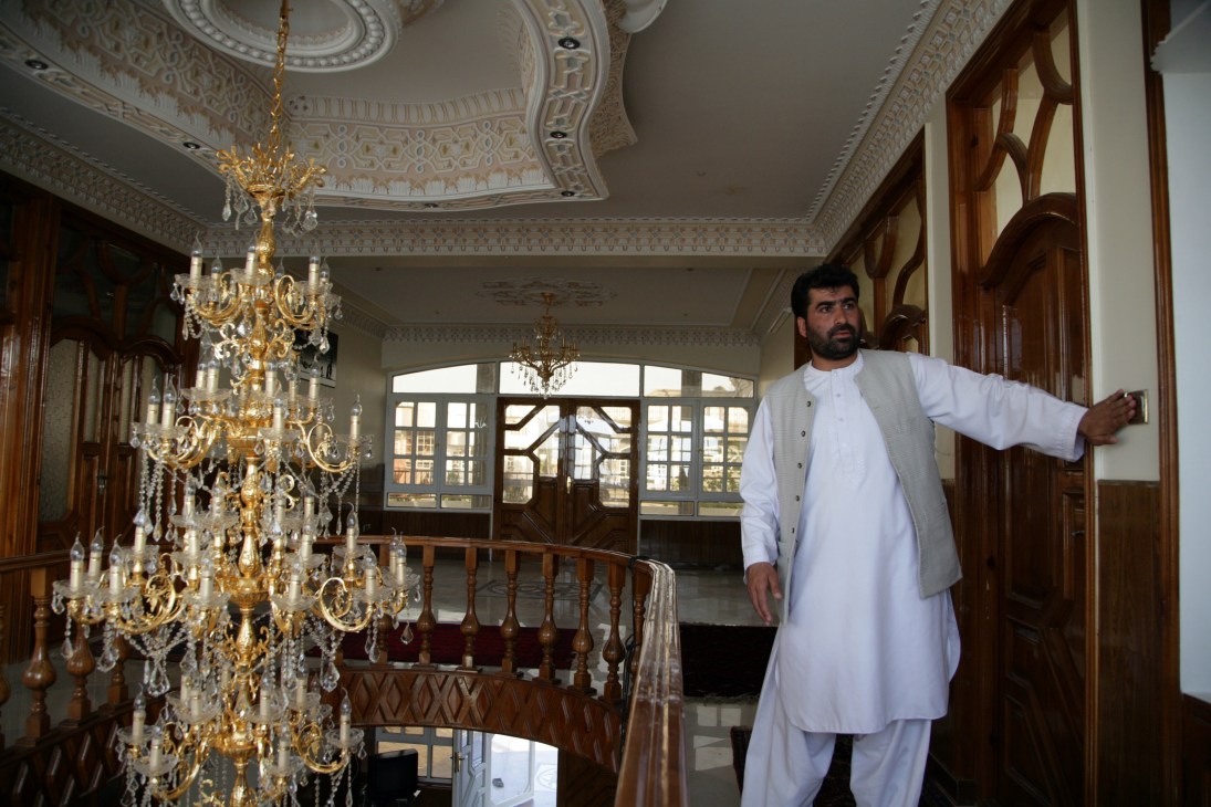 Man in white traditional Afghan clothing stands in ornate interior with large Italian crystal chandelier.