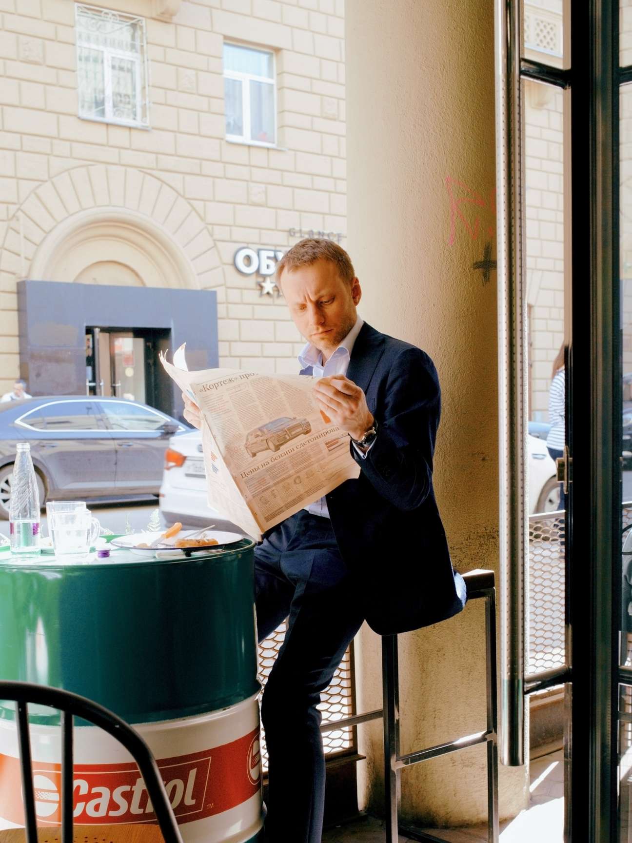 Man in business suit reading newspaper while standing at outdoor café table during lunch break