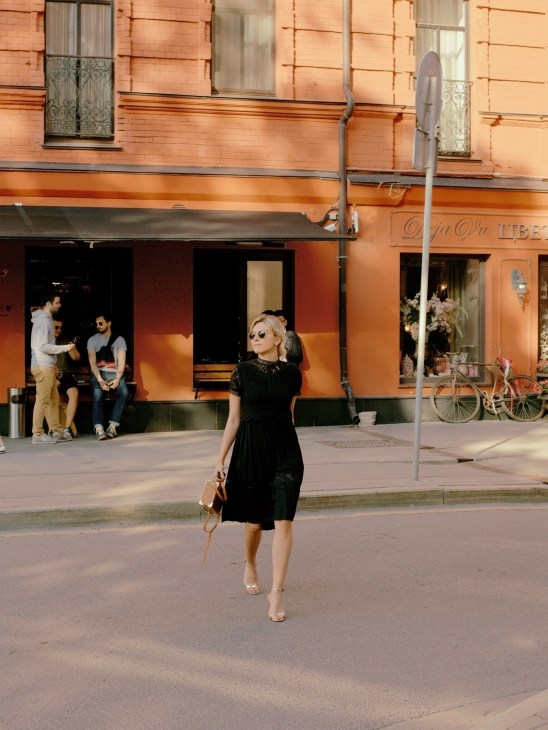 Woman in black dress walking on Moscow street with renovated orange building and shops in background