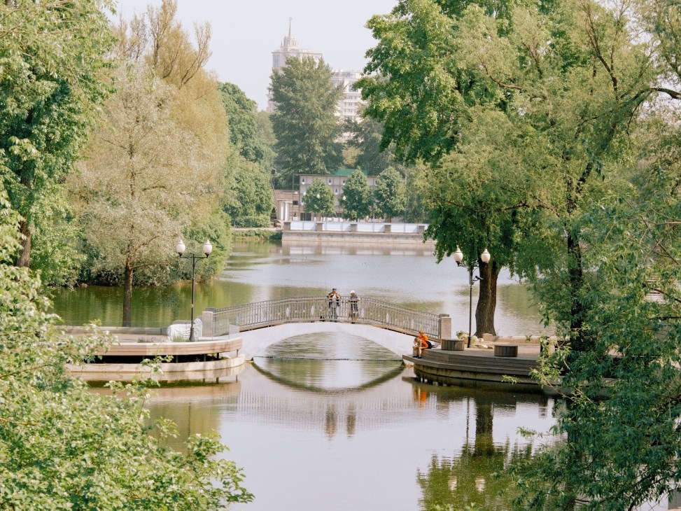 Golitsyn pond in Moscow with a curved bridge, trees, and historic buildings across the water.