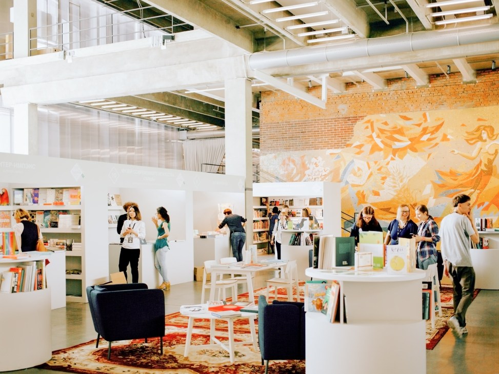 Visitors browsing at an art book fair inside a modern gallery space with exposed brick walls and contemporary artwork.