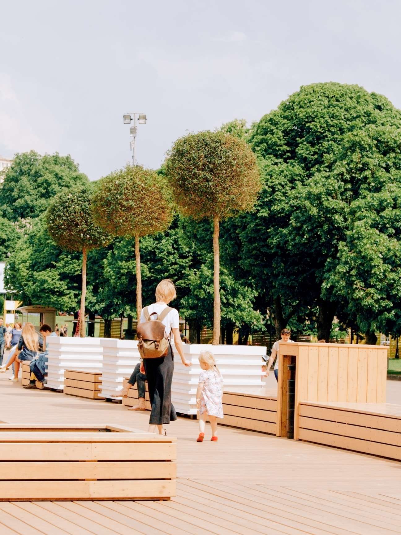 Woman and child walking on wooden deck in renovated Gorky Park with trees and seating in background.