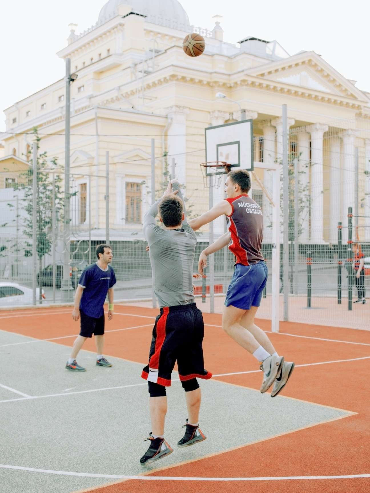 Basketball players shooting on a court in front of a white neoclassical synagogue in Moscow.