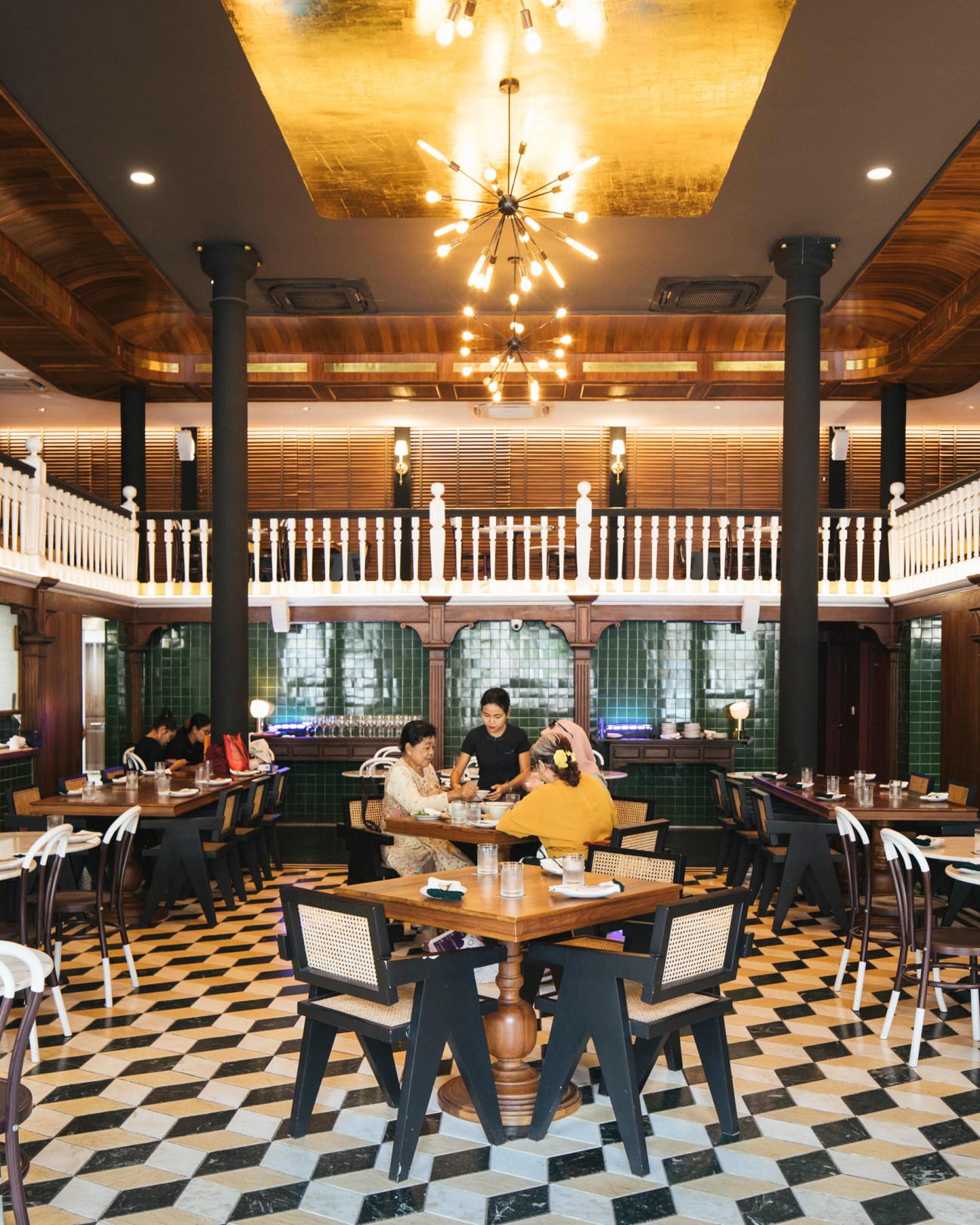 Diners seated at tables in an elegant restaurant with checkered floors, wooden furniture, and colonial-style architecture