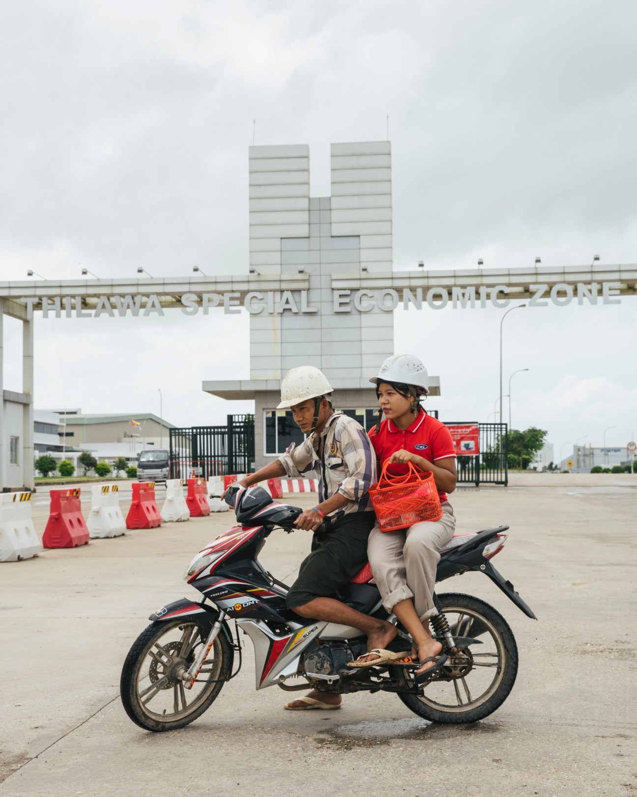 Two people on a motorcycle outside the entrance gate of Thilawa Special Economic Zone