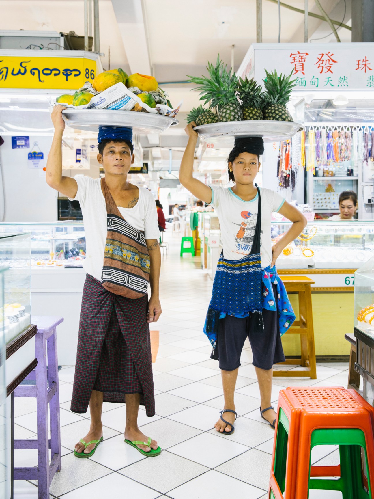 Two women carrying trays of fruit on their heads in a market