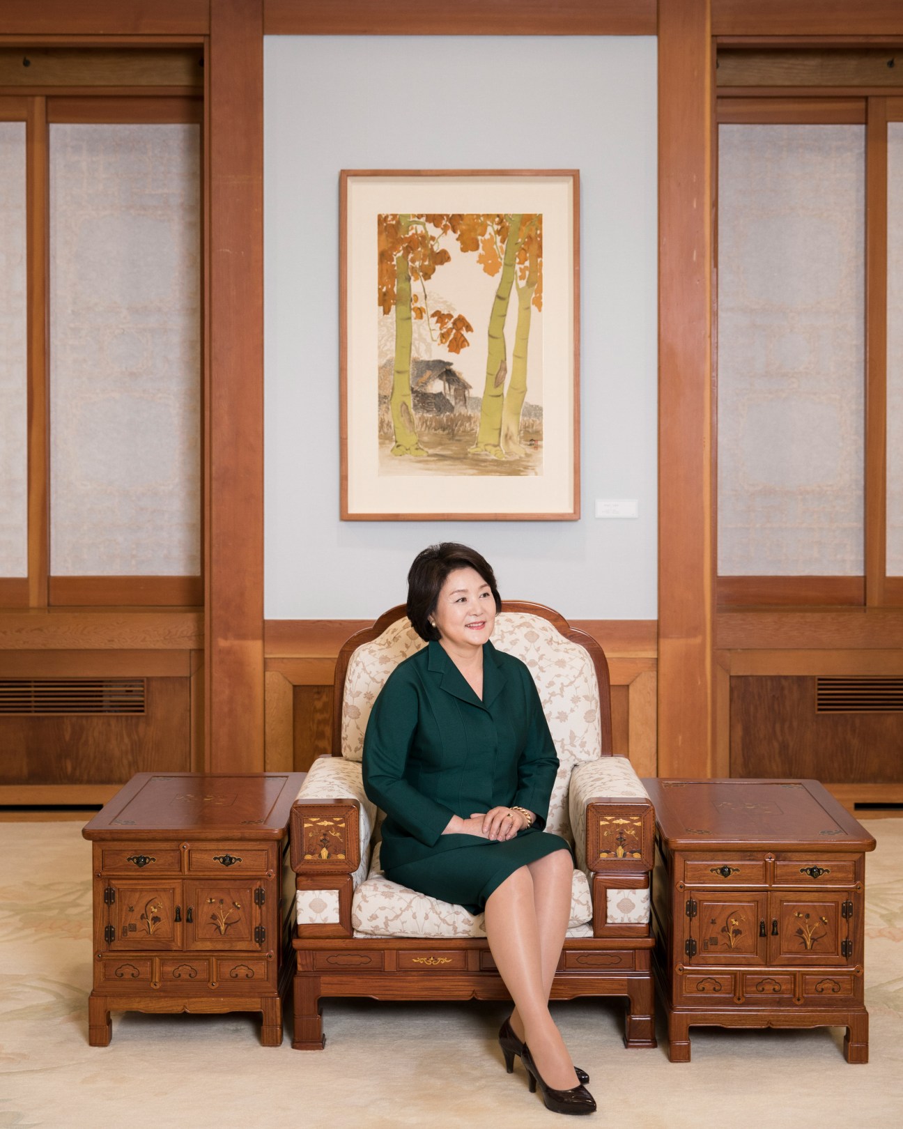 Kim Jung-sook, South Korea's First Lady, sits on a traditional wooden chair in an elegant room with framed artwork on the wall behind her.