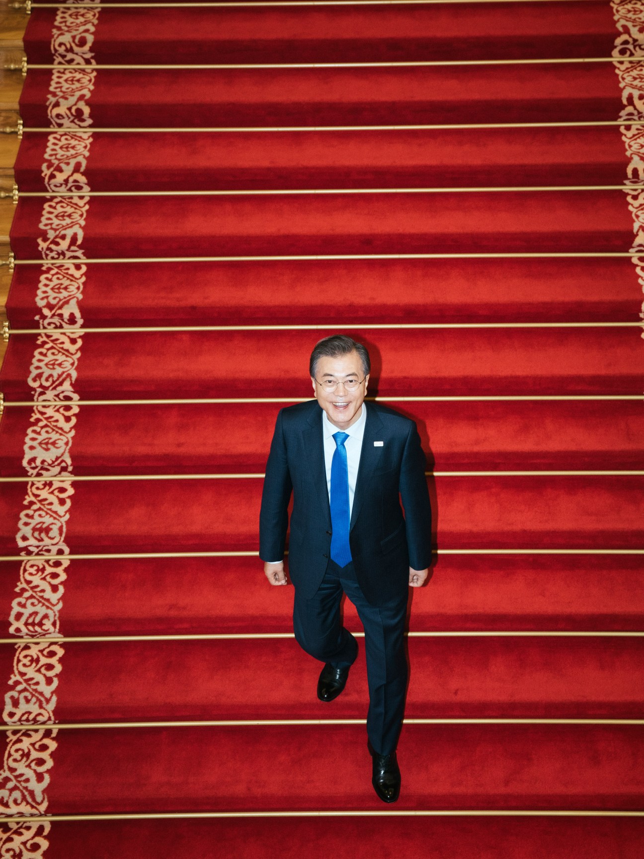 South Korean President Moon Jae-in walking down a grand red carpet staircase.
