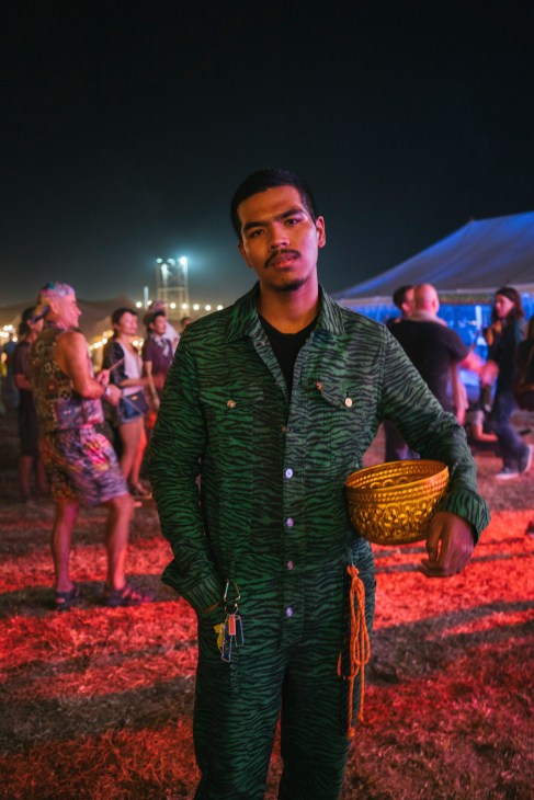 Man in tiger-pattern boiler suit holding a golden bowl at Wonderfruit festival at night.