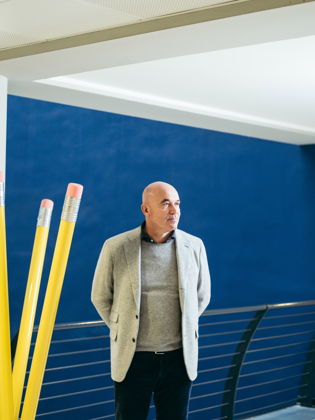Fila CEO Massimo Candela stands against a blue wall next to oversized yellow pencils.