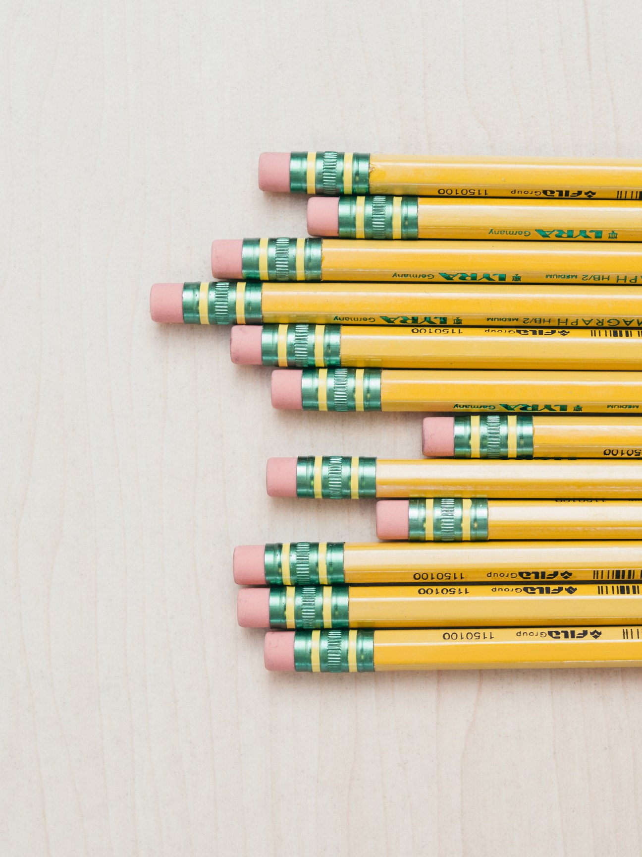 Yellow pencils with pink erasers and green ferrules arranged in diagonal rows on white background.