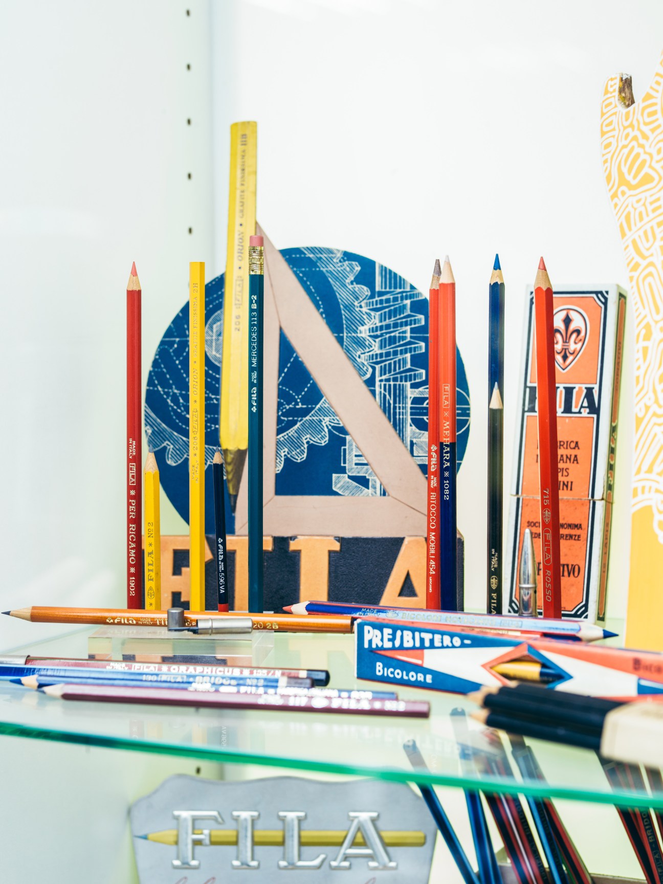 Assorted vintage Fila pencils and art supplies arranged on a glass shelf with branded packaging visible.