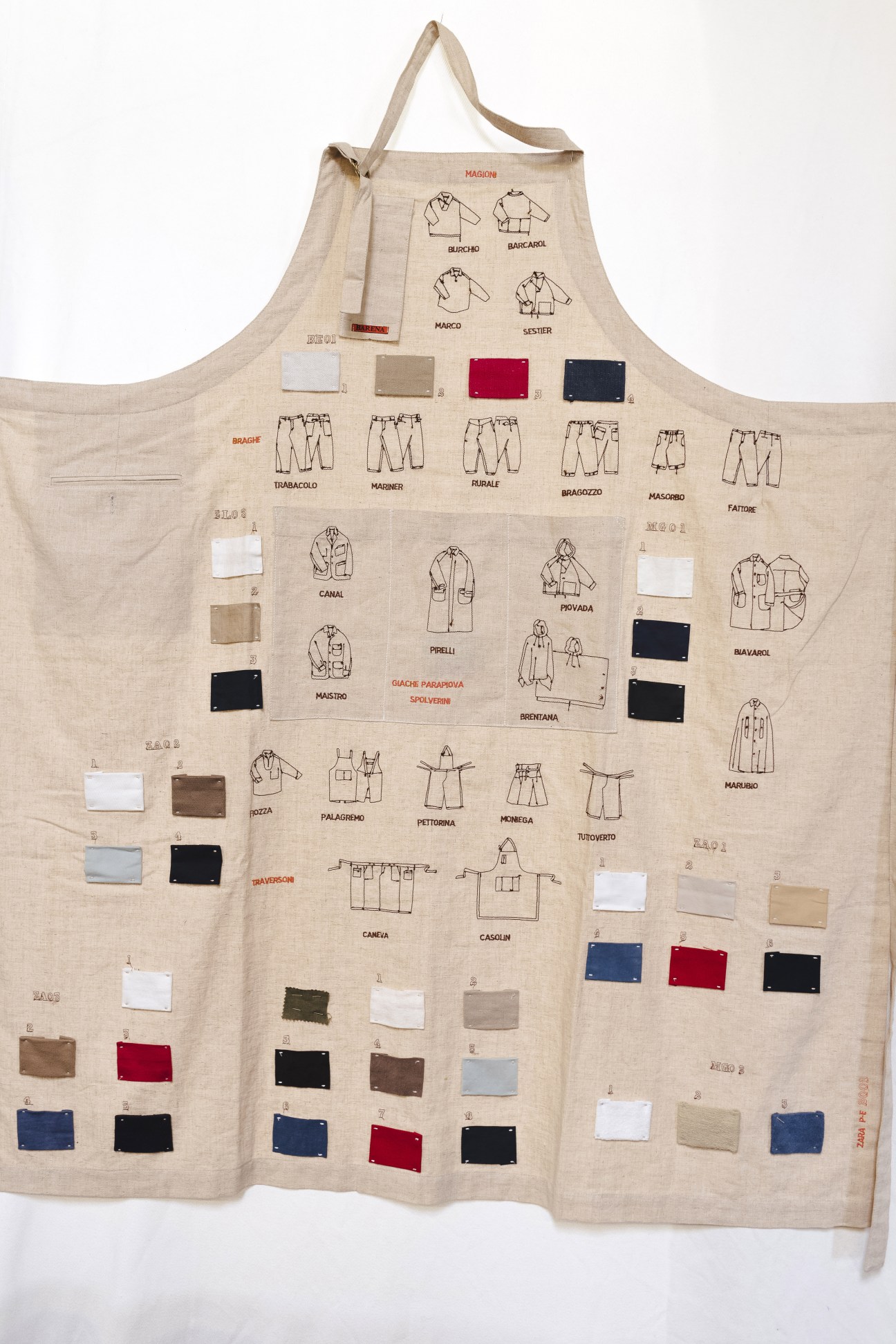 Cream linen apron embroidered with sketches of clothing items and fabric swatches, representing Barena's inaugural 2001 collection.