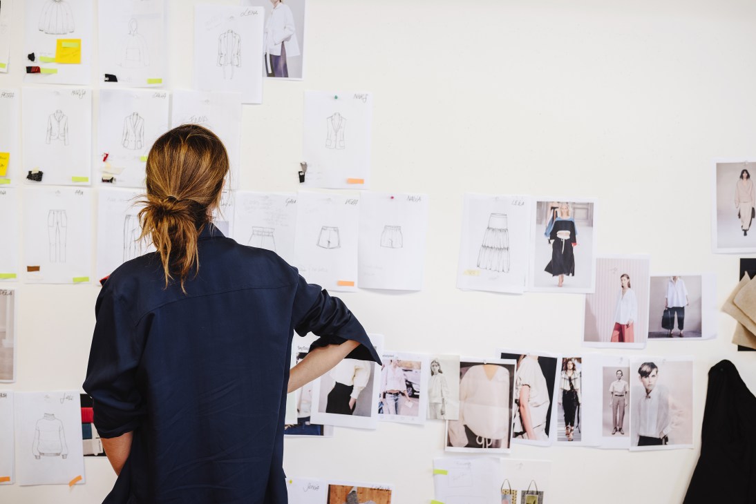 Designer reviewing fashion sketches and mood boards pinned to a studio wall.