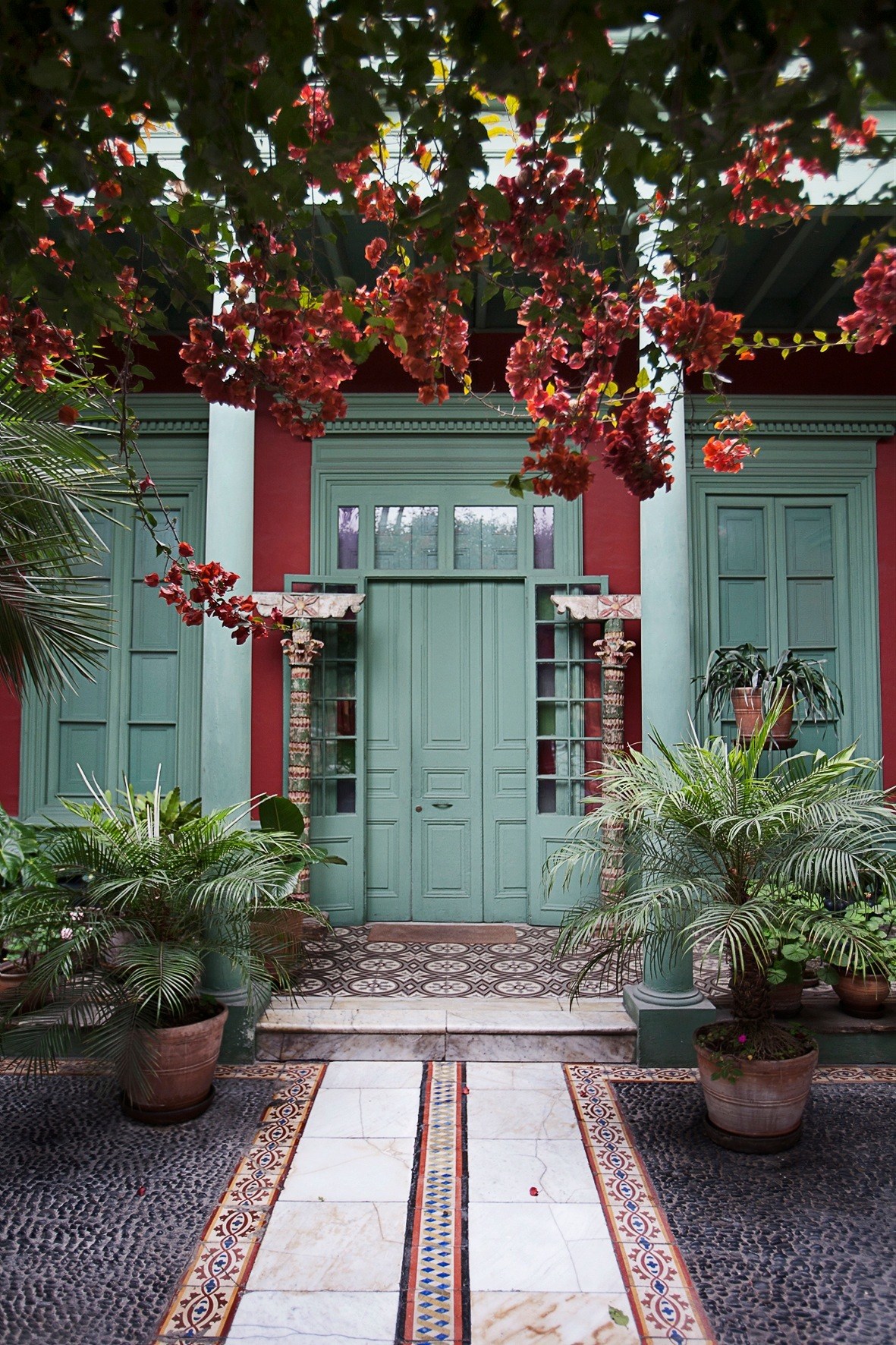 Colonial house courtyard with red bougainvillea flowers, turquoise doors and potted palms in Barranco, Lima.