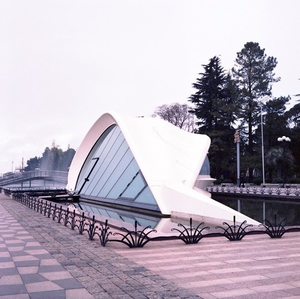 Modern white sculptural structure in Batumi's Seaside Park with patterned pavement and trees.