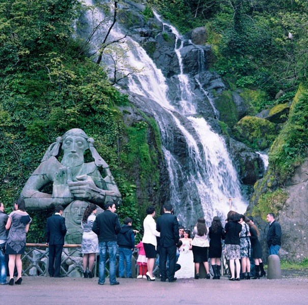 Wedding party gathered in front of a stone statue of St Andrew with a waterfall cascading in the background.