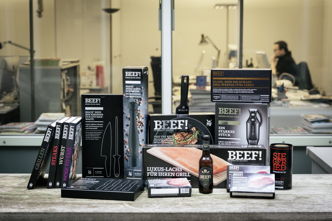 Various Beef! branded products displayed on a table including cookbooks, knives, beer, and packaged meats.