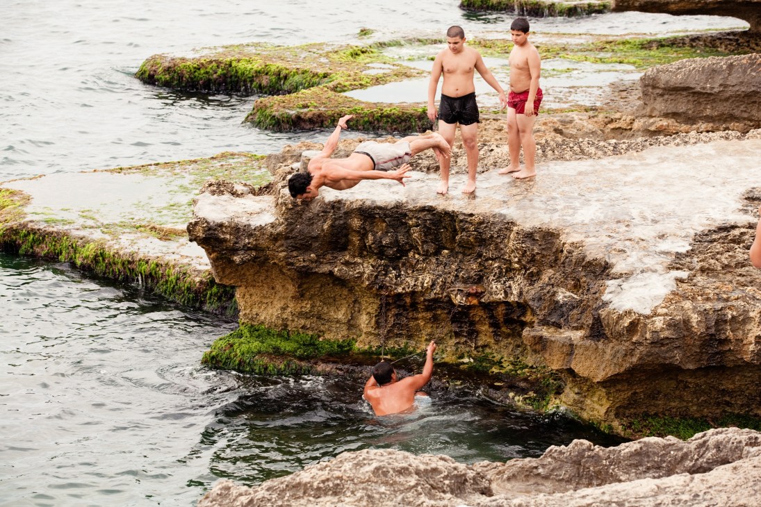 Young men swimming and diving off moss-covered rocks into the sea at Heybeliada in the Princes' Islands.