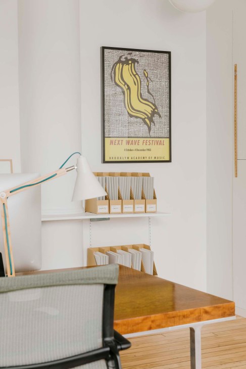Roy Lichtenstein's signed Next Wave Festival poster displayed on a white wall above office shelving.
