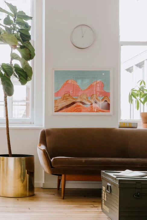 Modern office interior with brown sofa, framed abstract landscape artwork, potted plant, and minimalist décor.