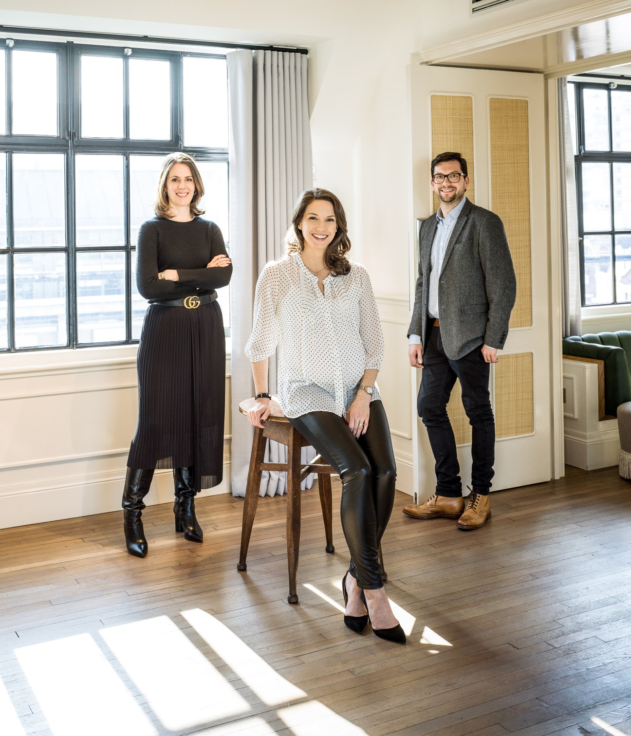 Three gallery directors pose in a bright, modern interior space with large windows.