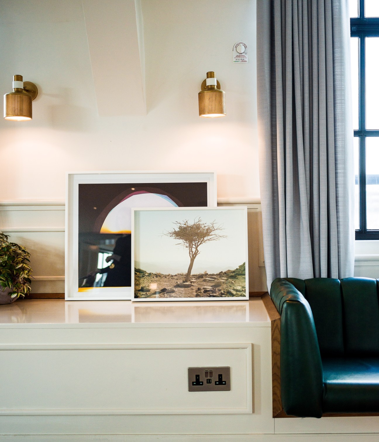 Framed photographs displayed on a white shelf: a desert landscape with a solitary tree in the foreground, and an abstract image with circular light.