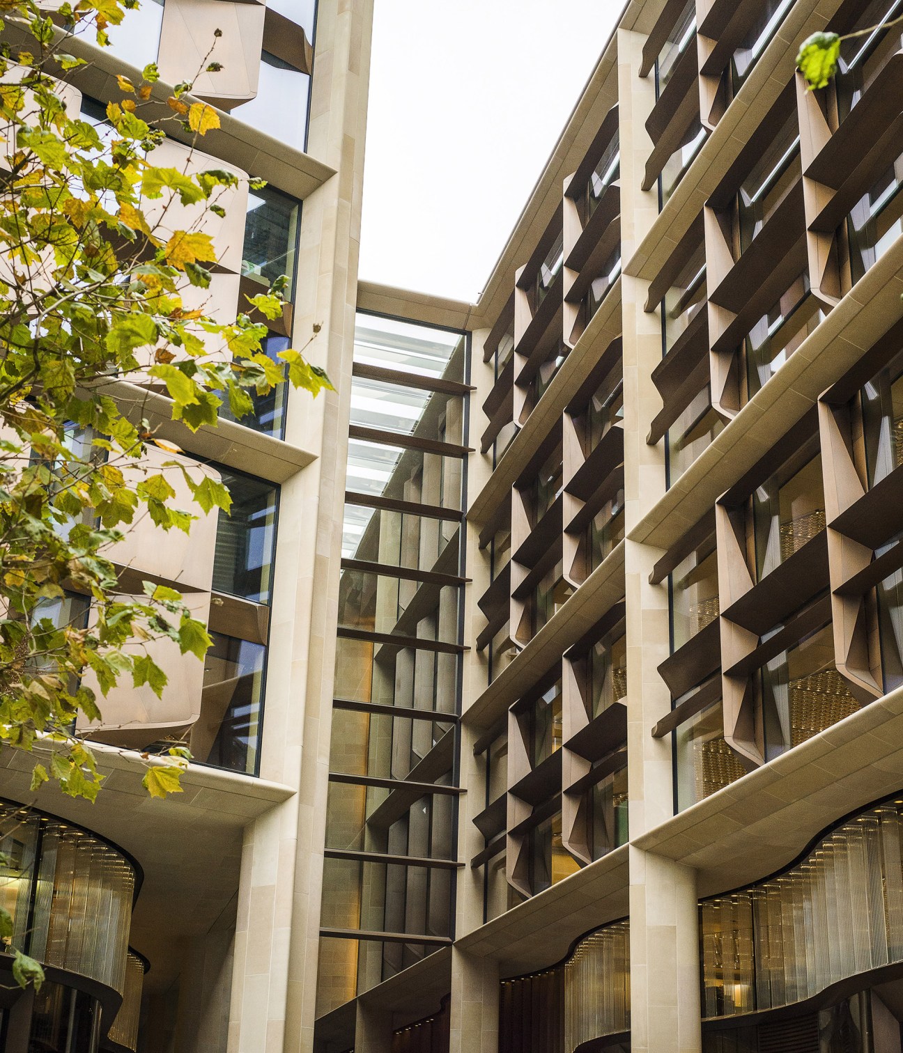 Exterior detail of Bloomberg building showing Derbyshire sandstone and hand-patinated bronze façade with green foliage.