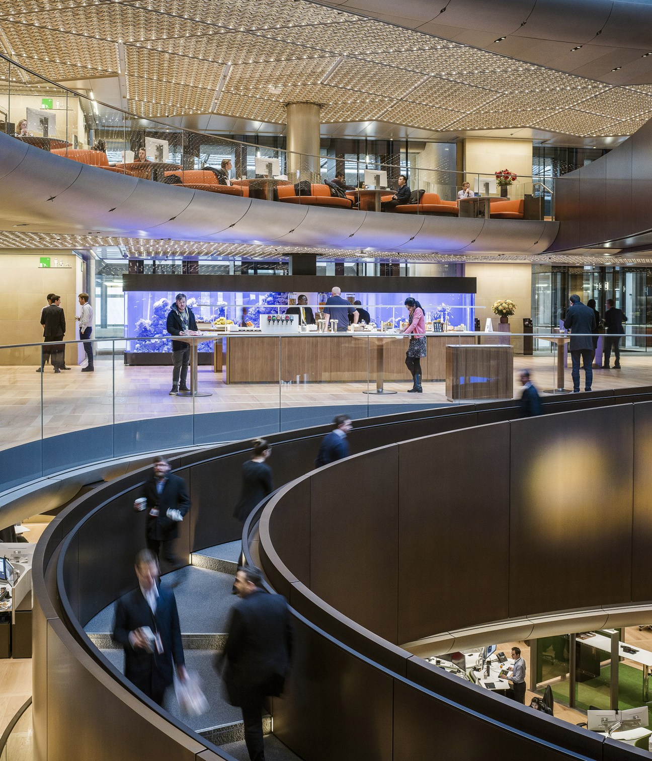 Wide sweeping ramp in Bloomberg headquarters with people walking and conversing across multiple floor levels.