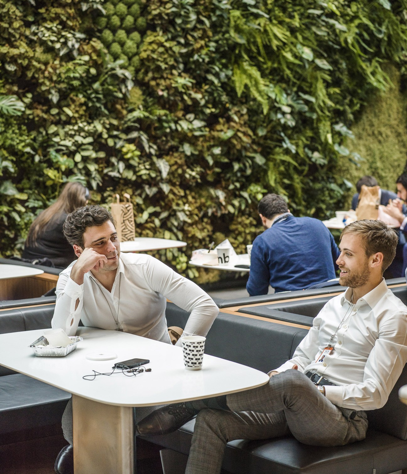 Two men in white shirts conversing at a table in Bloomberg's Pantry with a living green wall behind them.
