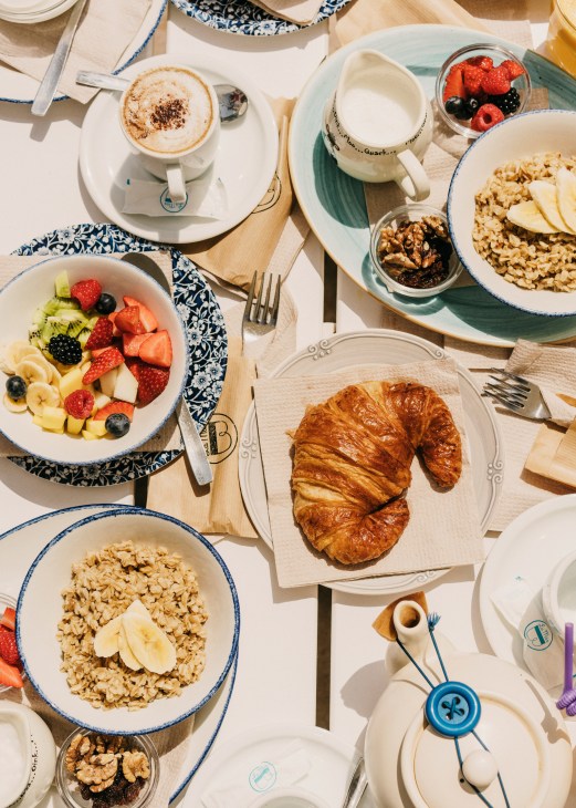 Overhead view of a breakfast spread at La Más Bonita featuring croissants, oatmeal, fresh fruit, yogurt and coffee.