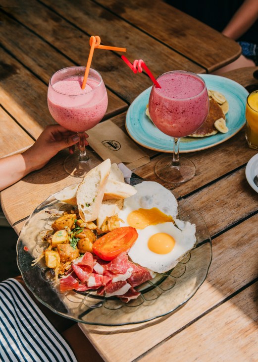 Breakfast spread at La Más Bonita featuring eggs, jamón, potatoes and bread with pink smoothie cocktails.