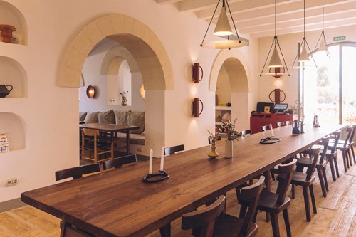 Dining room with long wooden table, chairs, arched white walls and pendant lights